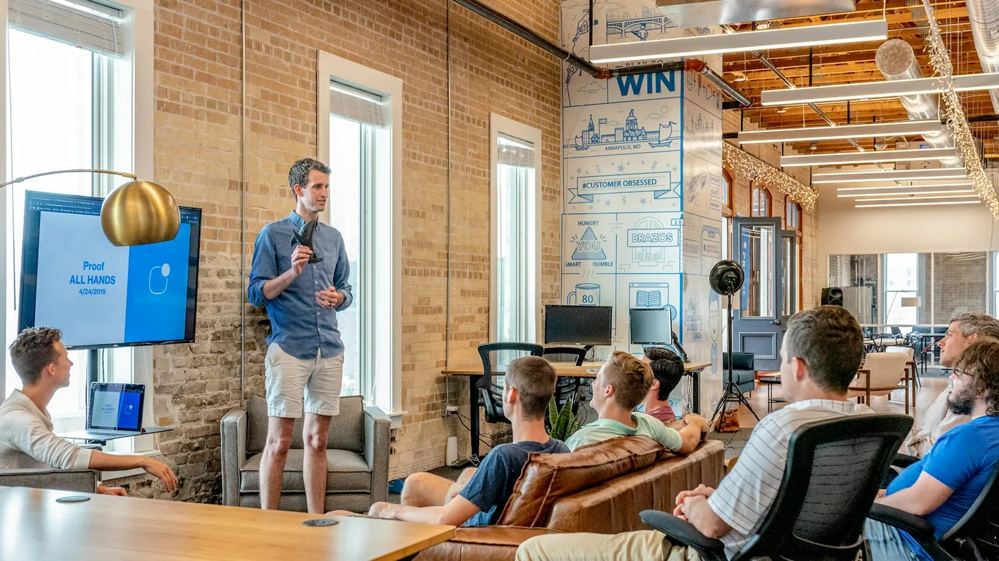 A presenter speaking to a team gathered in an open workspace